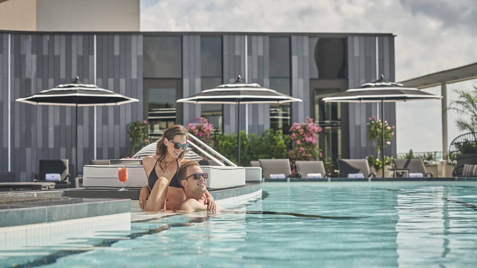 A man and woman relaxing at the edge of an outdoor pool.