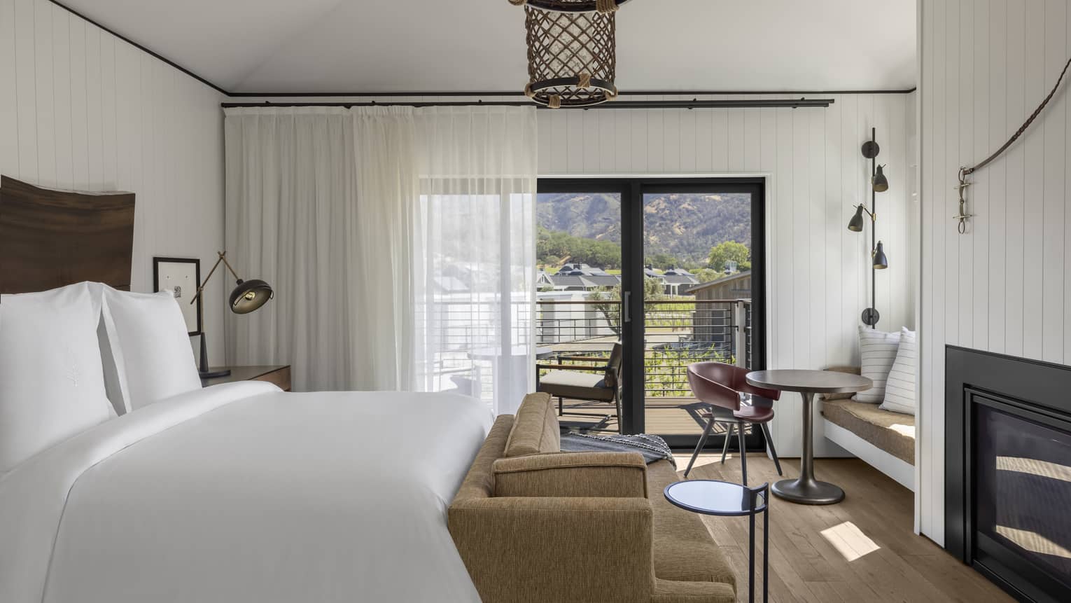 Bright resort bedroom with a king bed, sofa, fireplace, small dining area with built-in seating and sliding glass doors opening to a balcony with mountain views