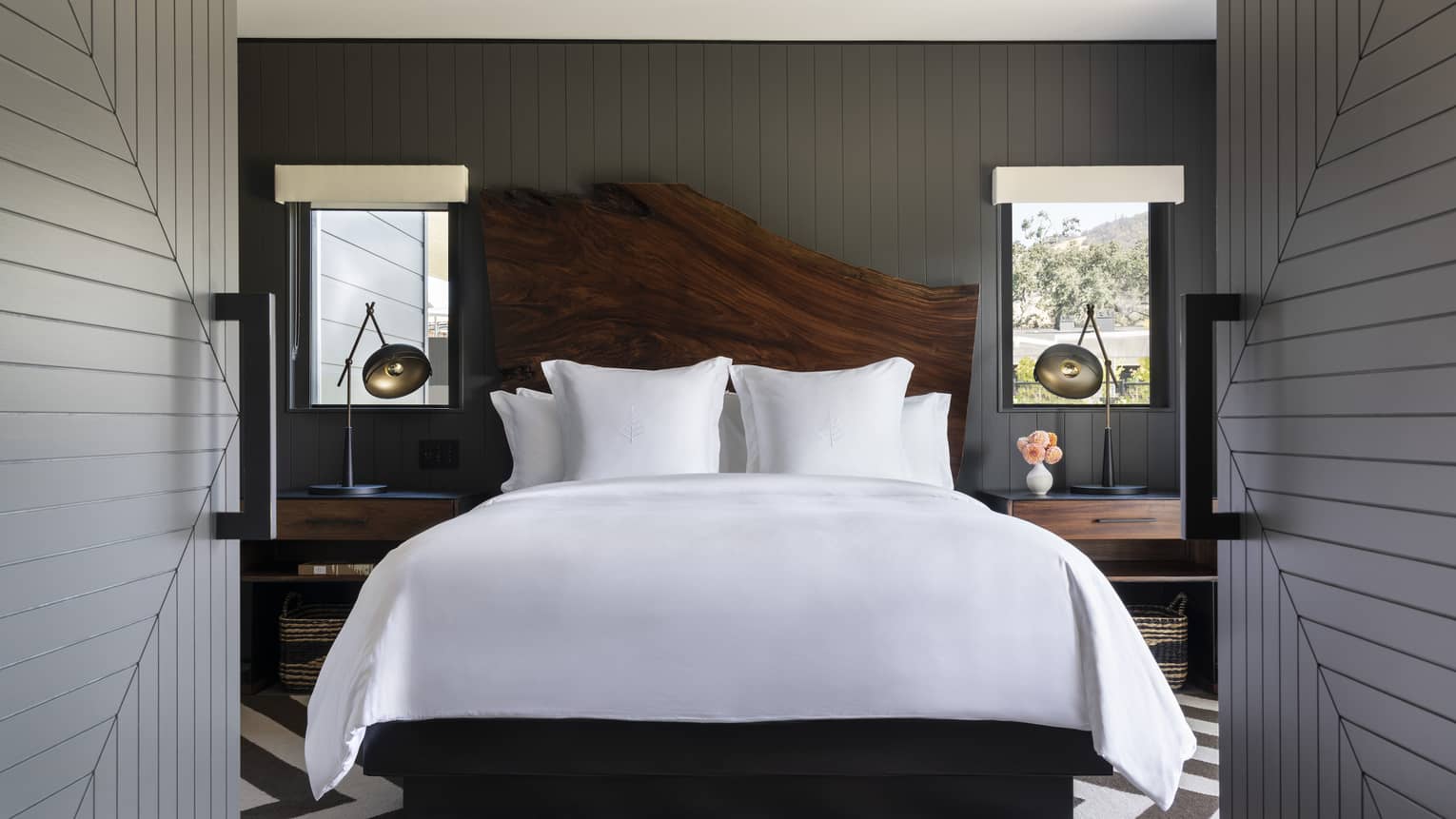 Luxury resort bedroom with a large white bed, wooden headboard and bedside tables with lamps in a dark-paneled room