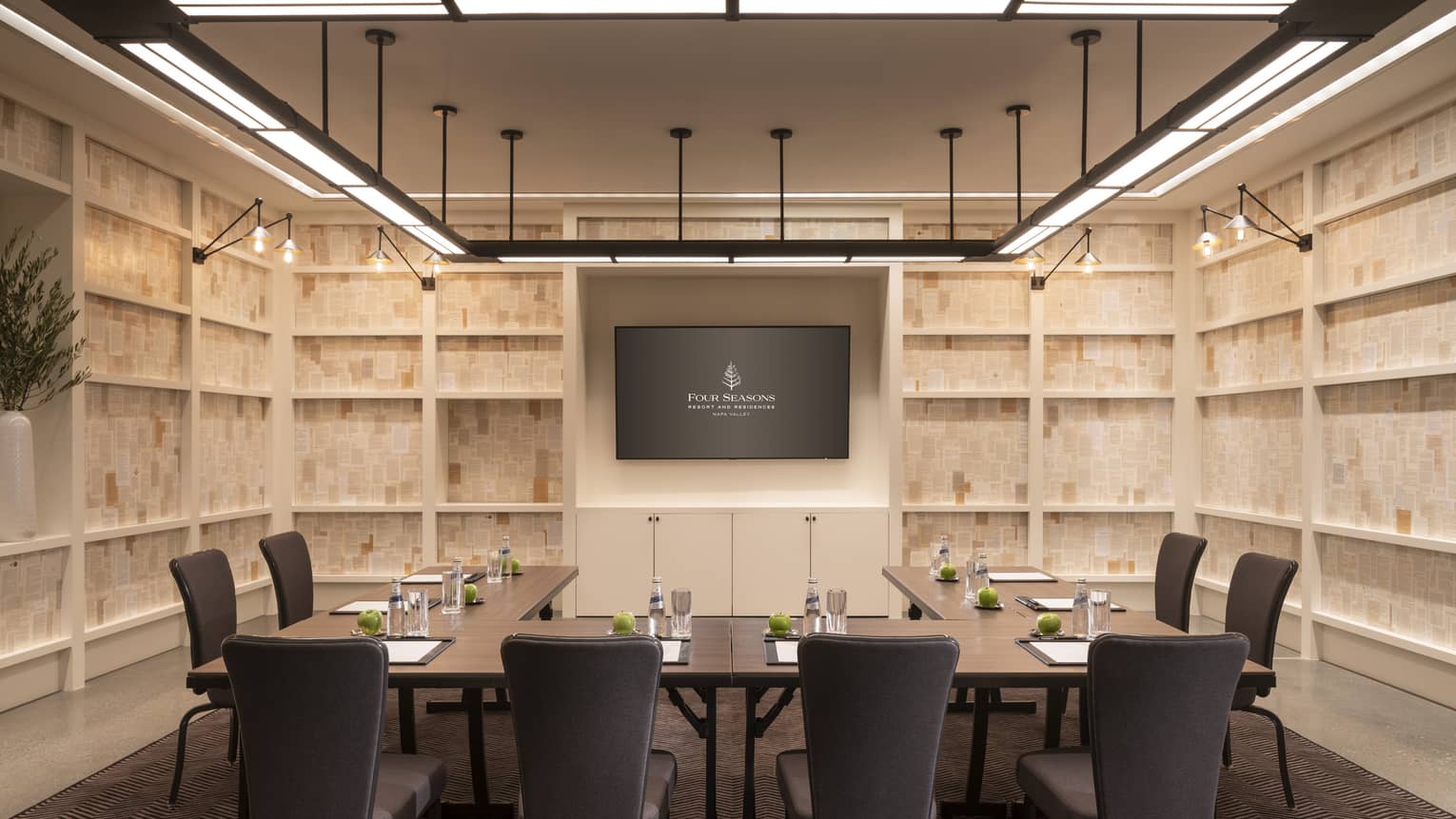 Private meeting room with light wood walls, TV screen on wall, l-shaped table
