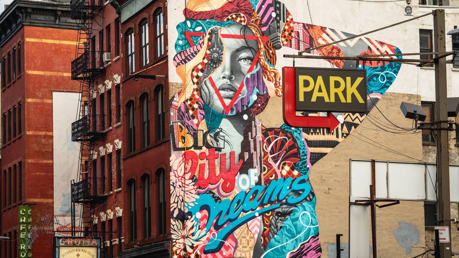A painted mural of a grey face and a colourful arm on the side of a red brick building.