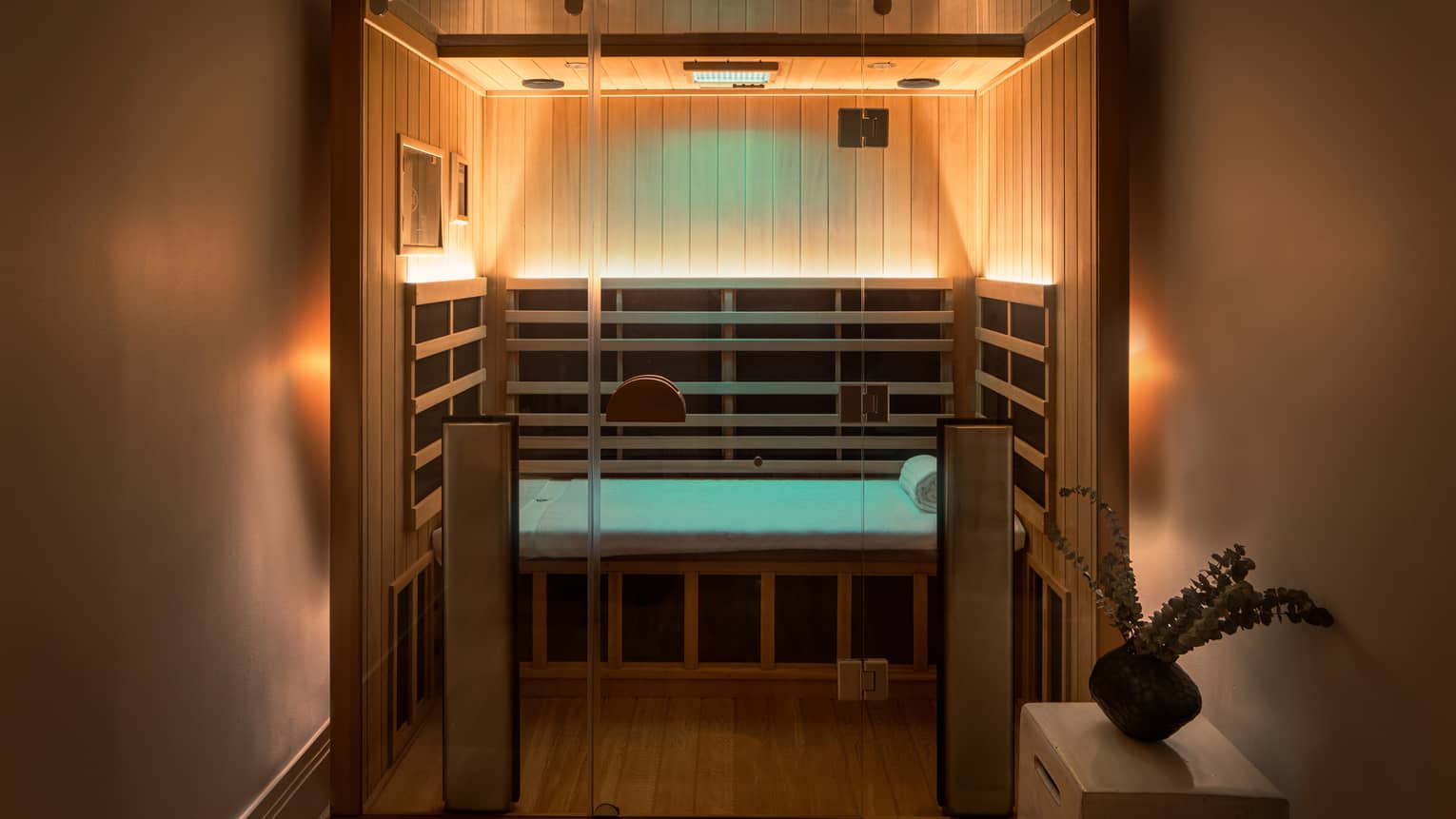 Wooden infrared sauna with lowlighting, side table with vase of eucalyptus