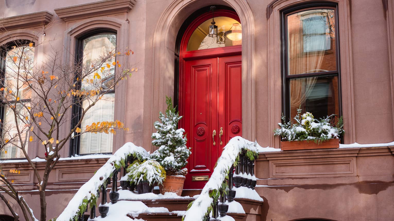 A red door with stairs covered in snow leading up to it.