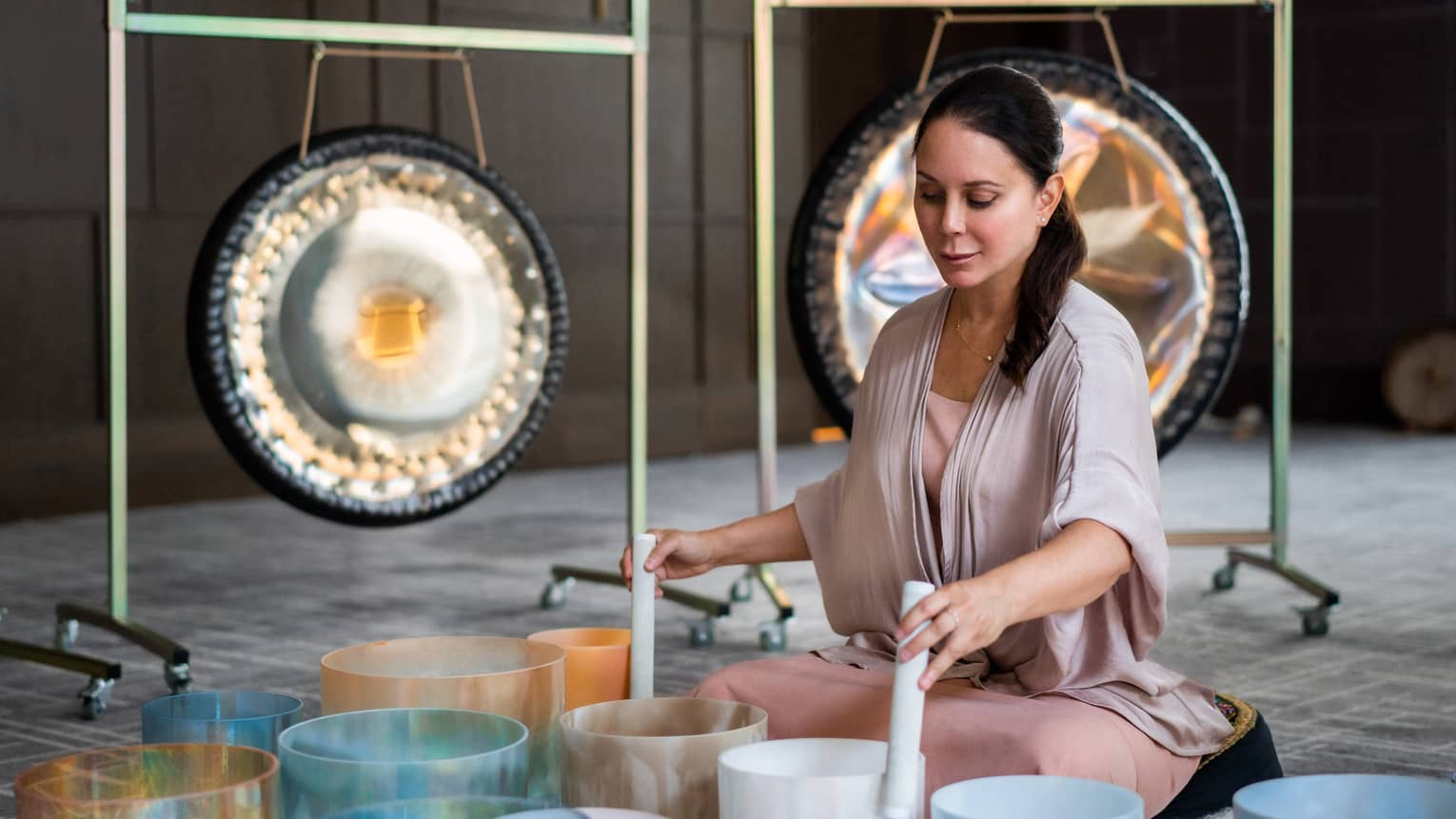 Michelle Pirret playing singing bowls in the foreground with two gongs in the background