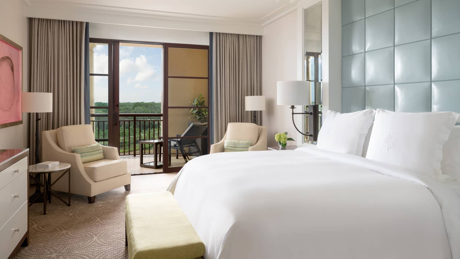 Hotel room with white king bed, light blue head board, beige armchair, walk-out balcony