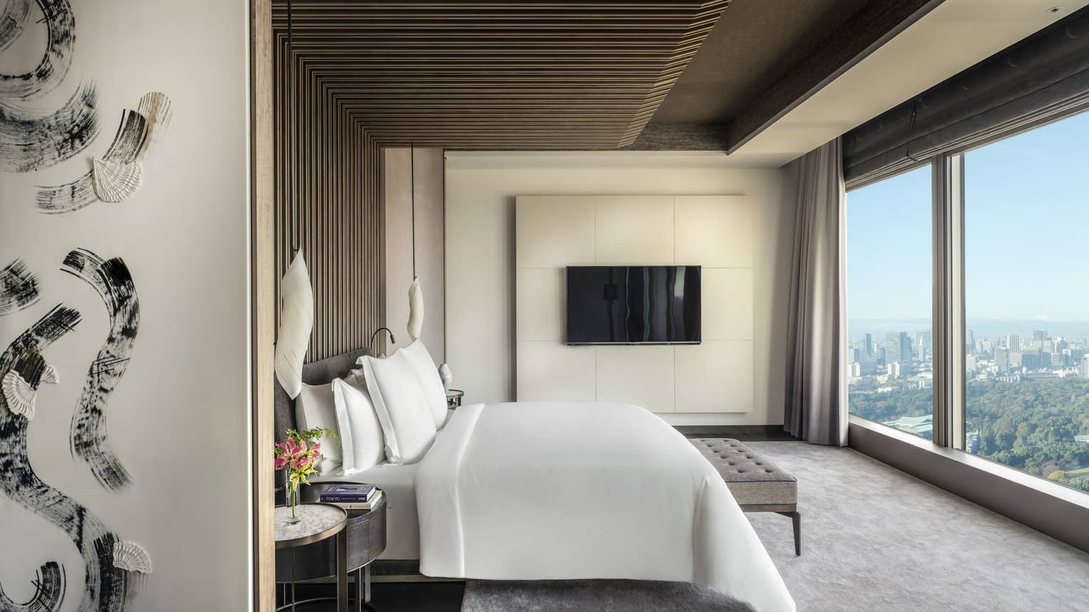Elegant bedroom with a king bed, TV, wooden ceiling accents, wall art and floor-to-ceiling windows offering expansive city views