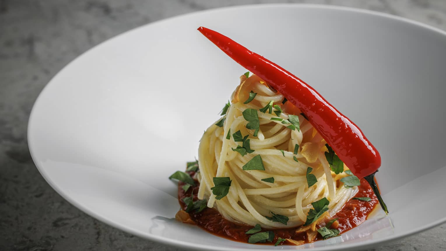 Twirled spaghetti dish in shallow white bowl topped with whole fresh chilli