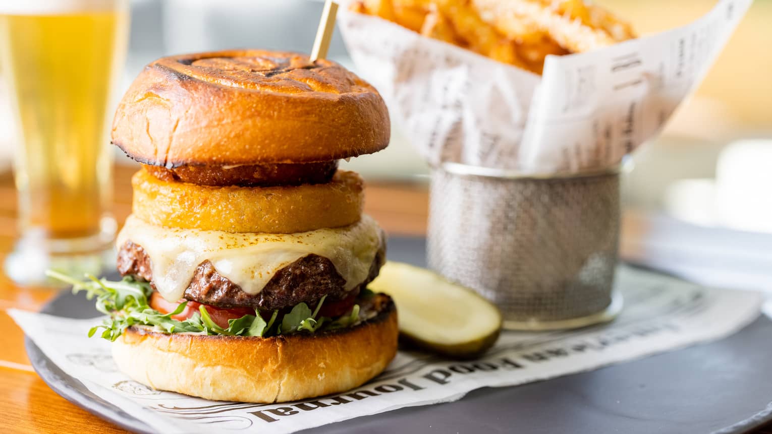 A burger next to a pickle and fries on a black plate.