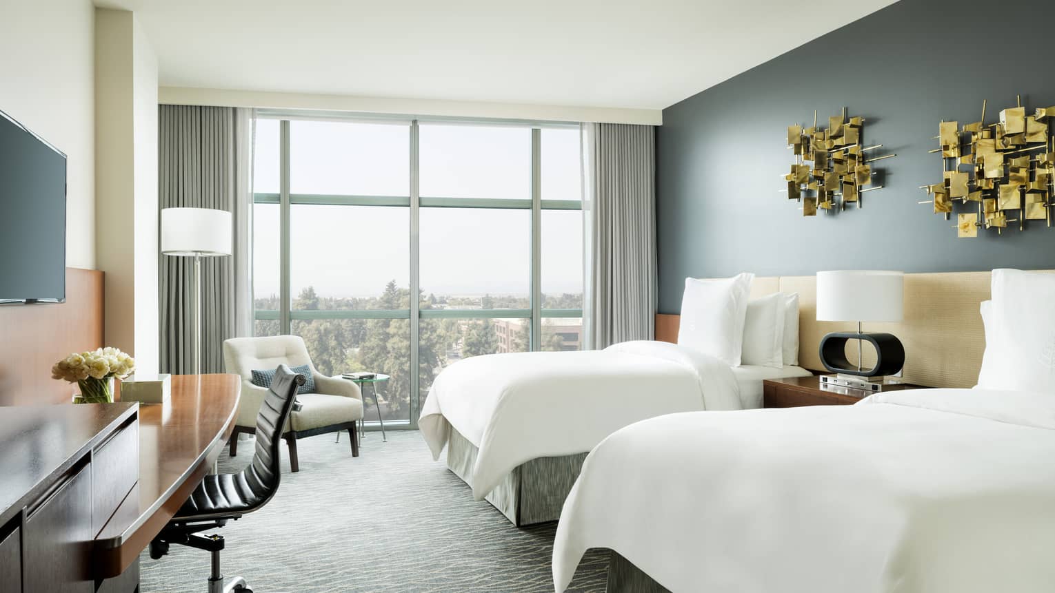 Deluxe Room double beds under modern gold art, desk under TV, armchair by window
