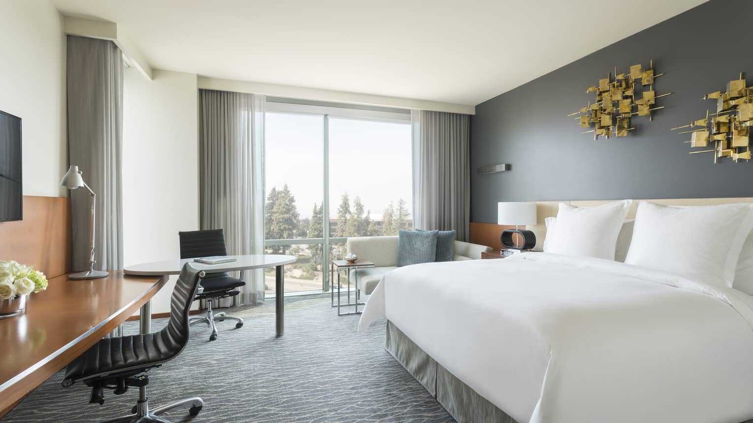 Deluxe Room bed under modern gold art, desks, chaise by window