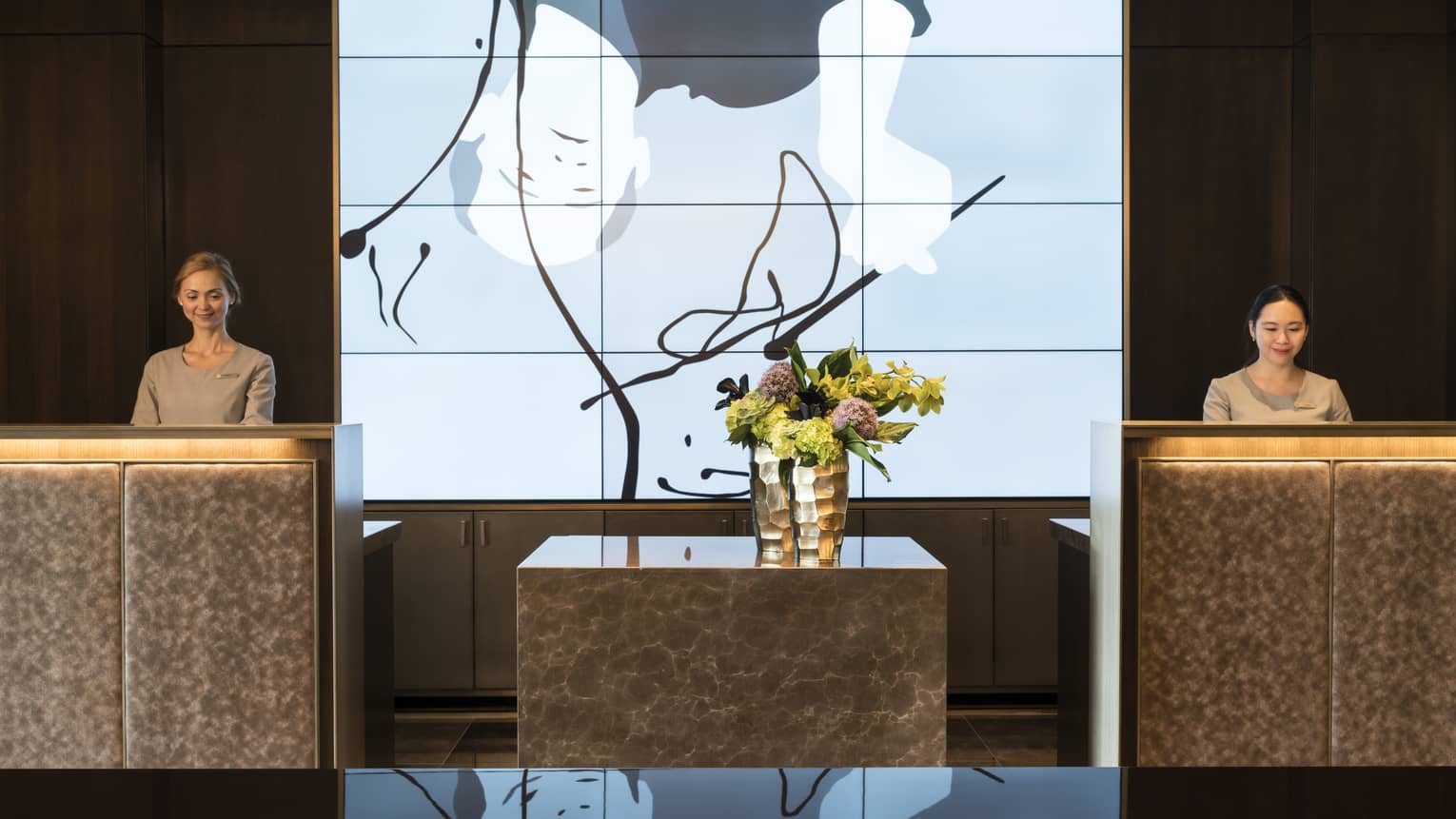 Digital art wall screens between two reception desks, staff in lobby