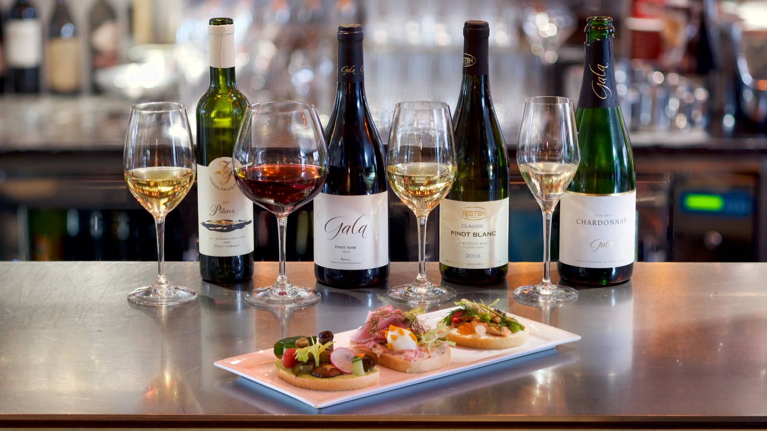 Wine tasting, four glasses and bottles, appetizer platter on bar 