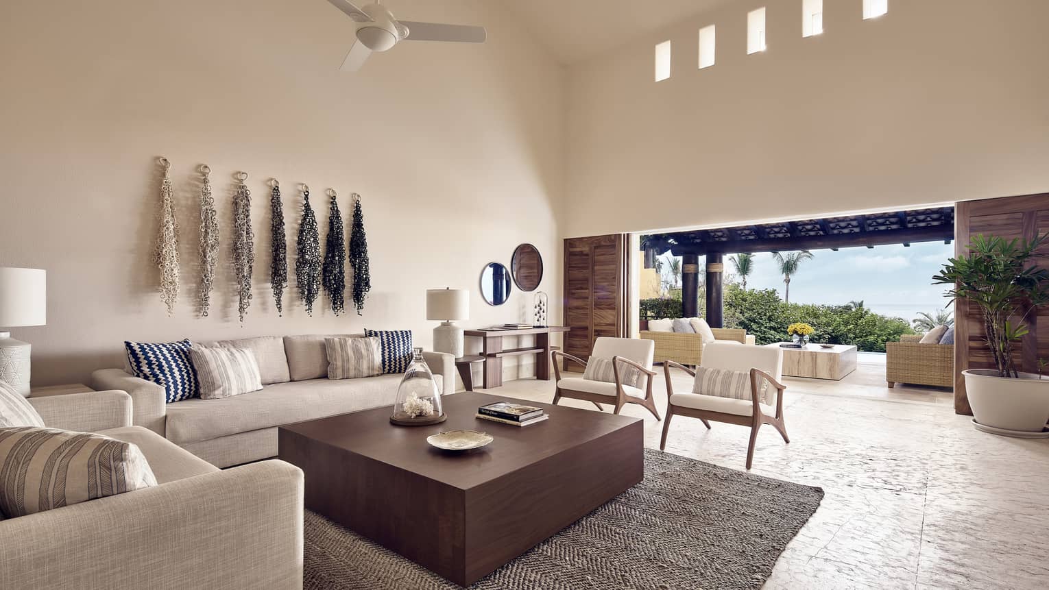 White linen sofas around large wood coffee table in bright living room, open patio wall