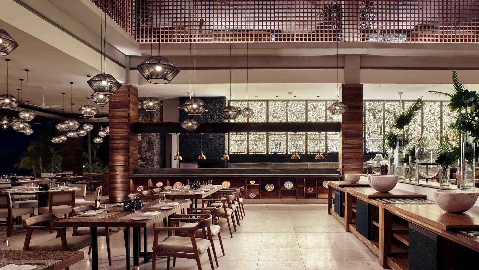 Wooden tables with palce settings are illuminated by light from black and white mosaic stain glass windows