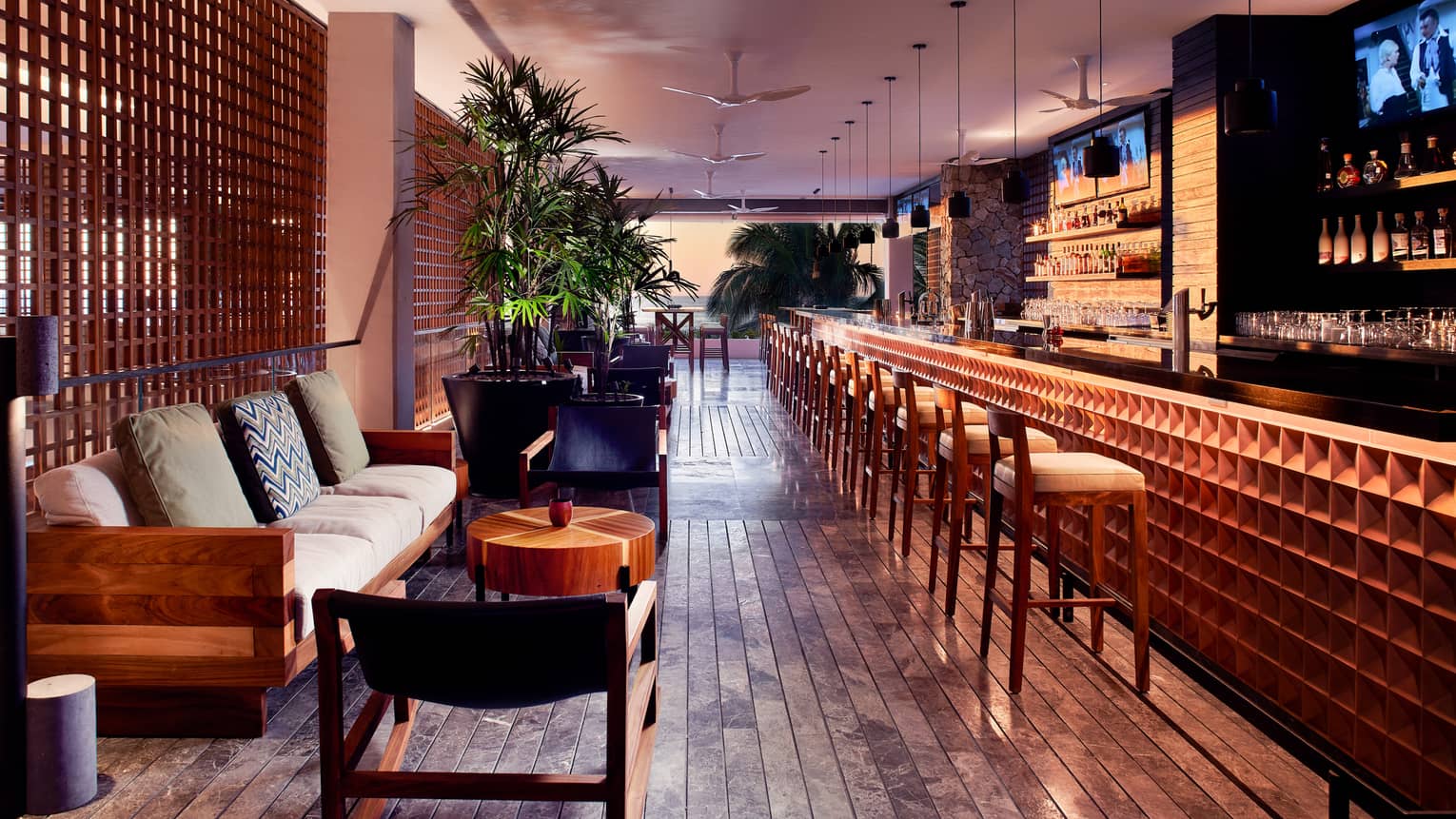 ,A dimly lit bar area with stools, chairs, and sofa.