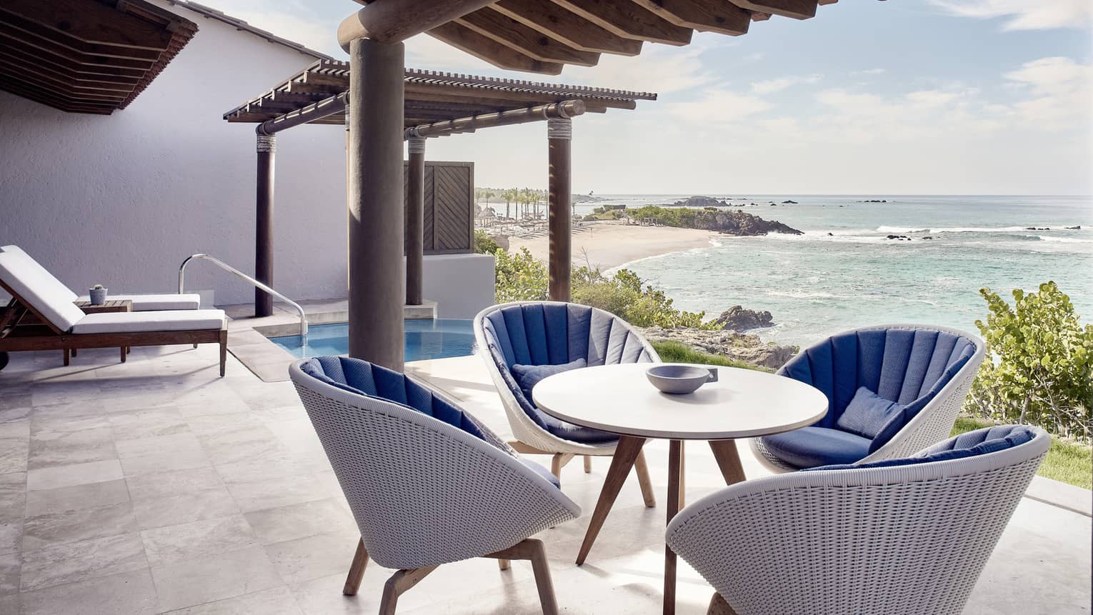 The private outdoor terrace of a modern suite near Puerto Vallarta, with ocean view and plunge pool, featuring a table and four white wicker chairs