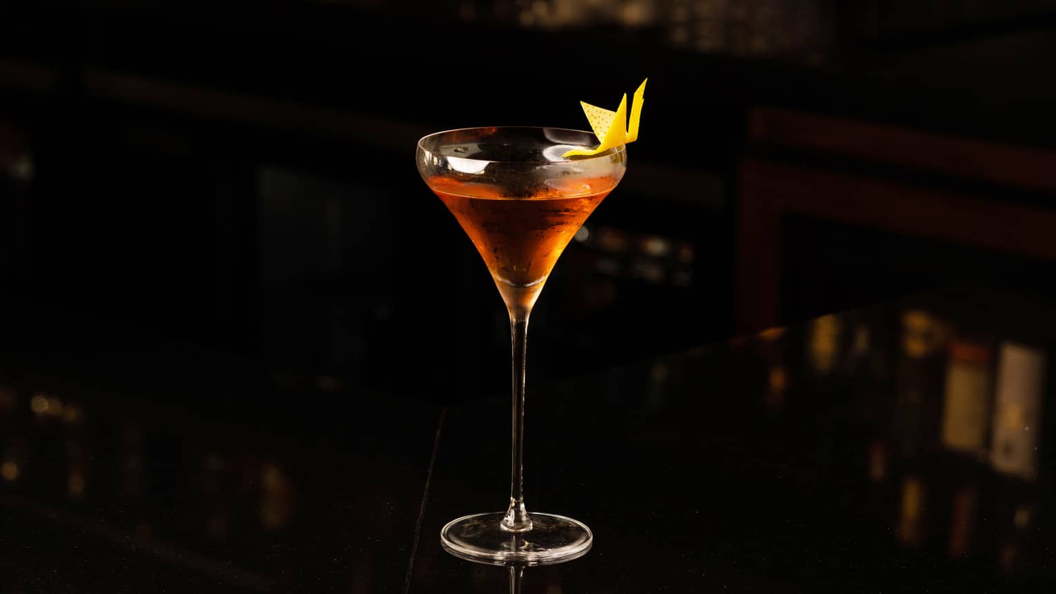 An amber coloured cocktail in a thin glass on a black background.