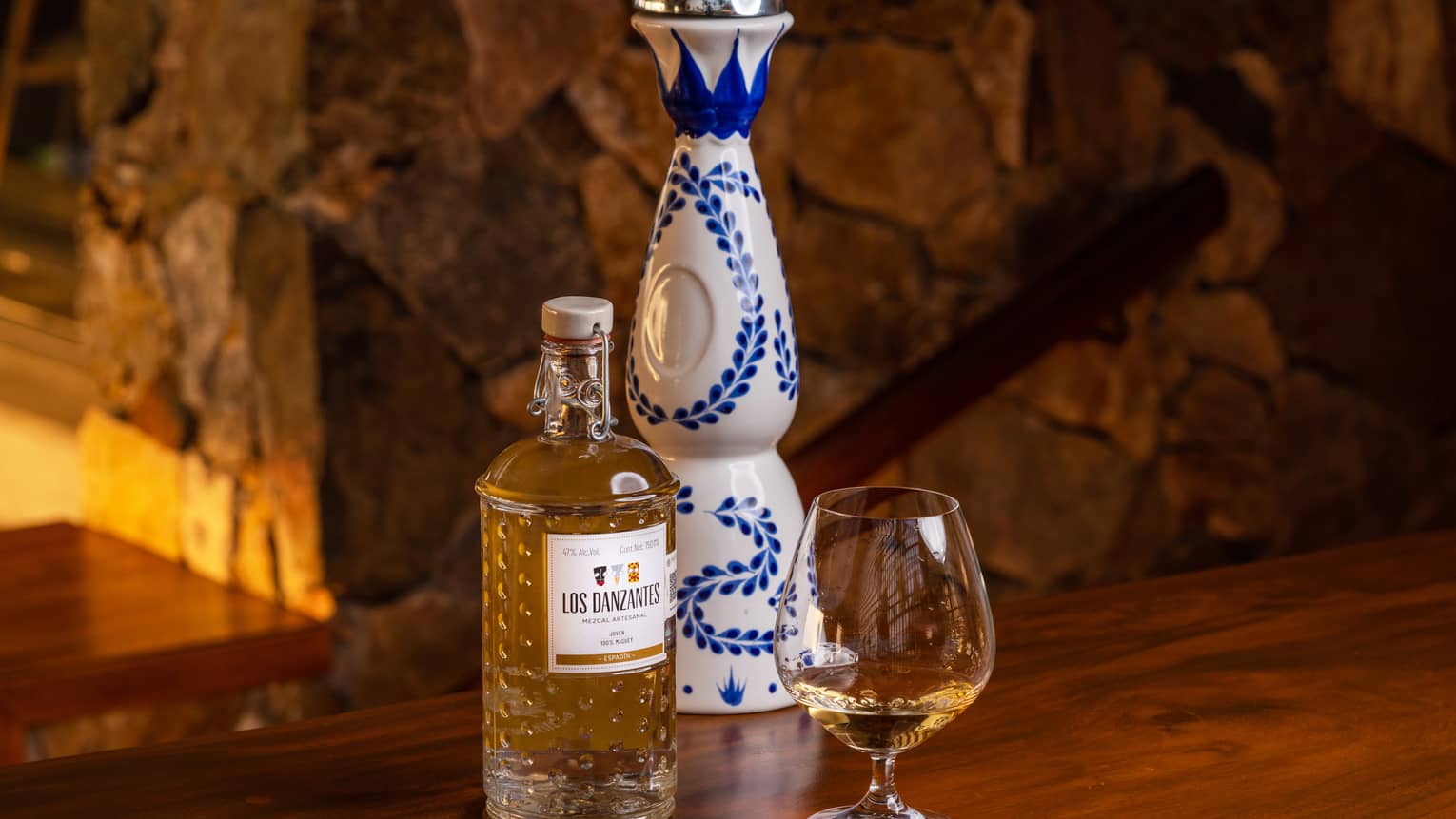A bottle of liquor next to a large container that is white and blue and a small glass.
