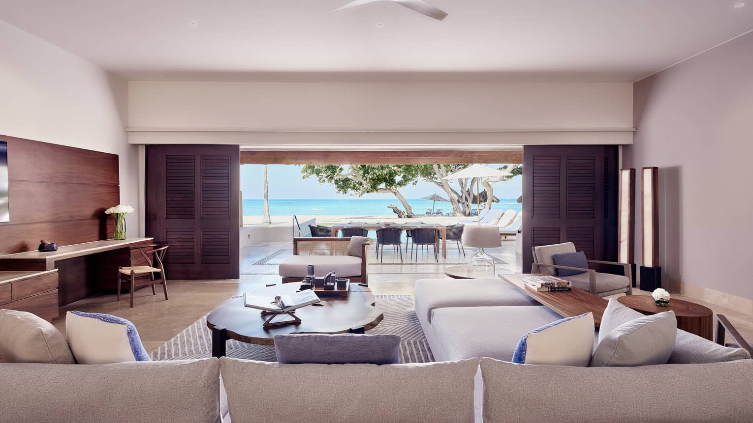 Arena Beach House living room with cream sectional sofa, large oak coffee table, doors open to outdoor dining area and pool