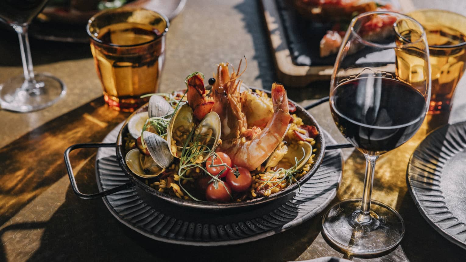 Paella dish on table with red wine glasses