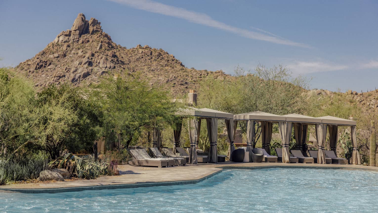 Pool with cabanas that have lounge chairs with a backdrop of the mountains.