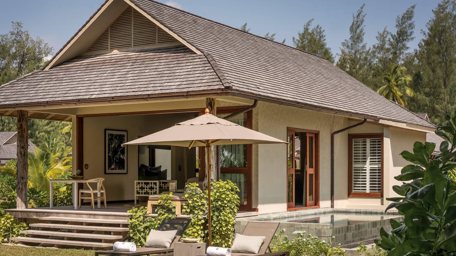 Exterior view of bungalow villa with two patio lounge chairs, umbrellas on lawn
