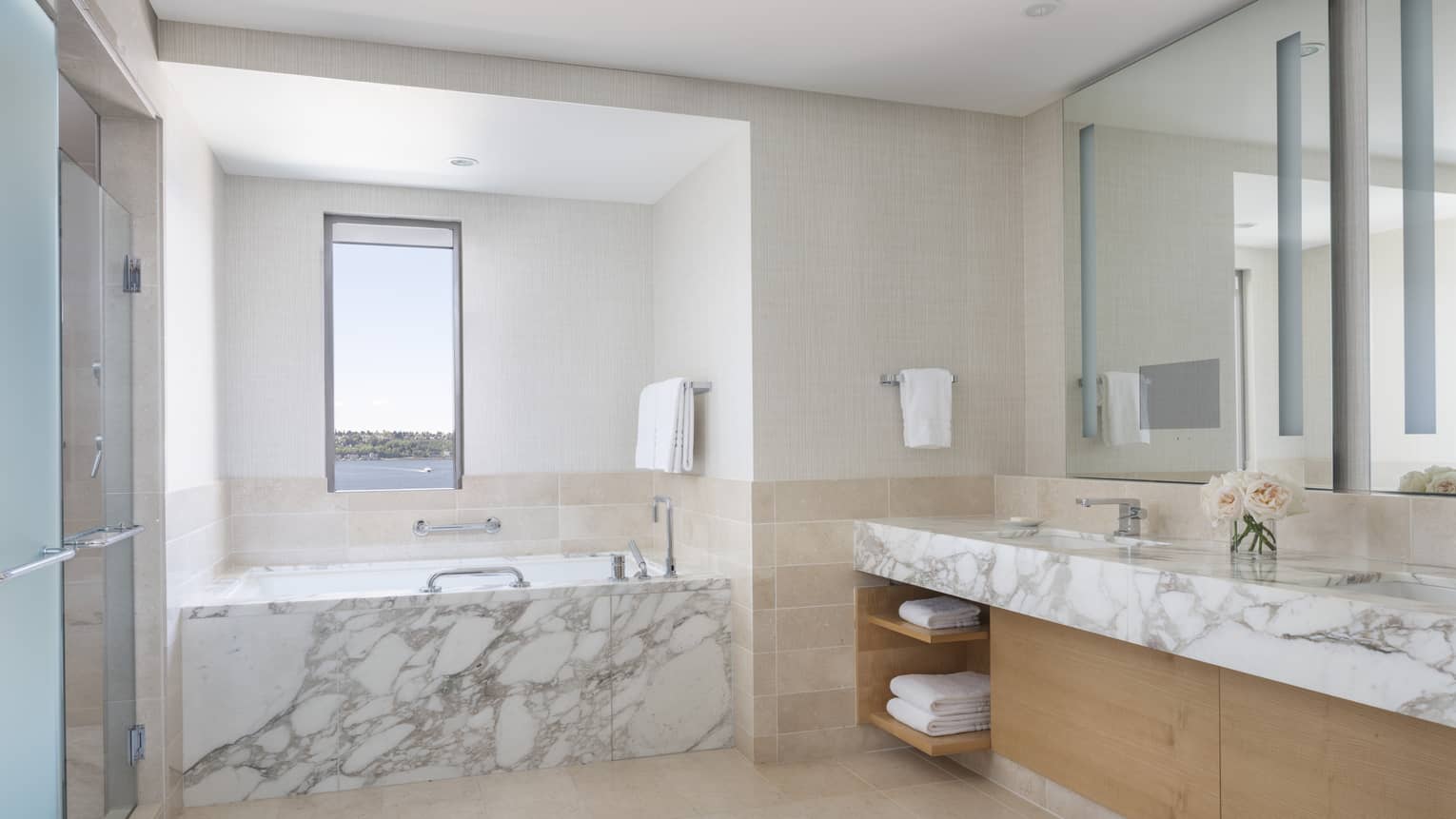 Marble countertops and a marble bathtub glow in the well-lit bathroom
