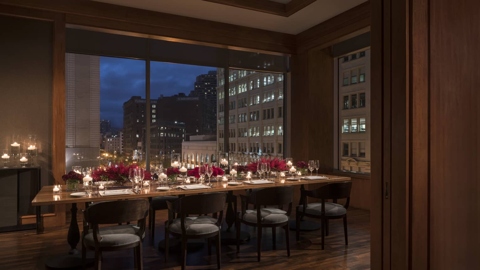 Long private dining table in dimly-lit room at night, set with wine glasses, elegant floral arrangements
