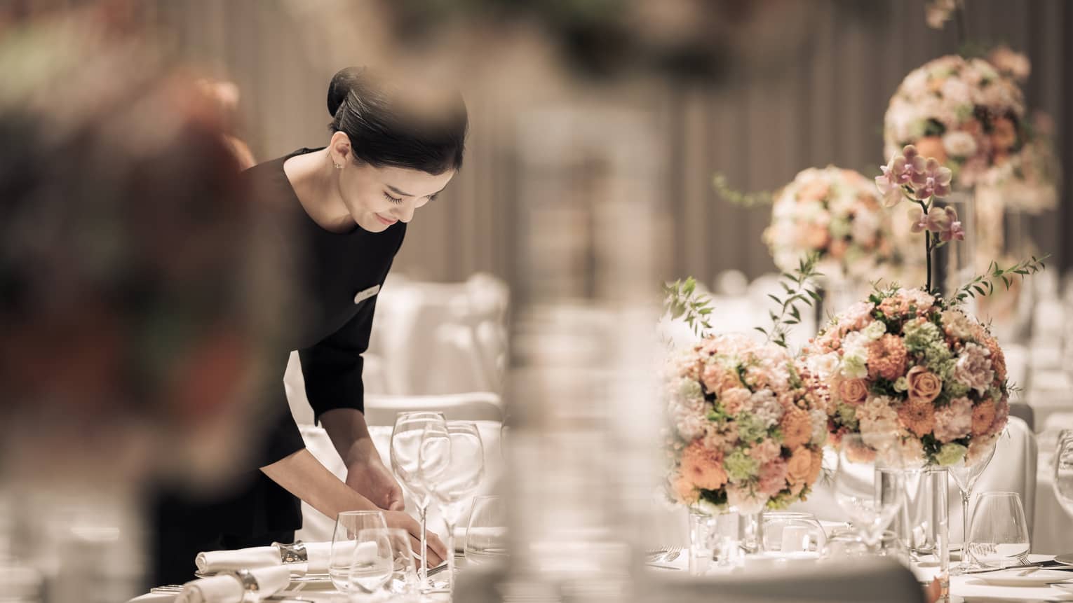 Hotel server sets formal banquet table with pink roses, flower arrangements