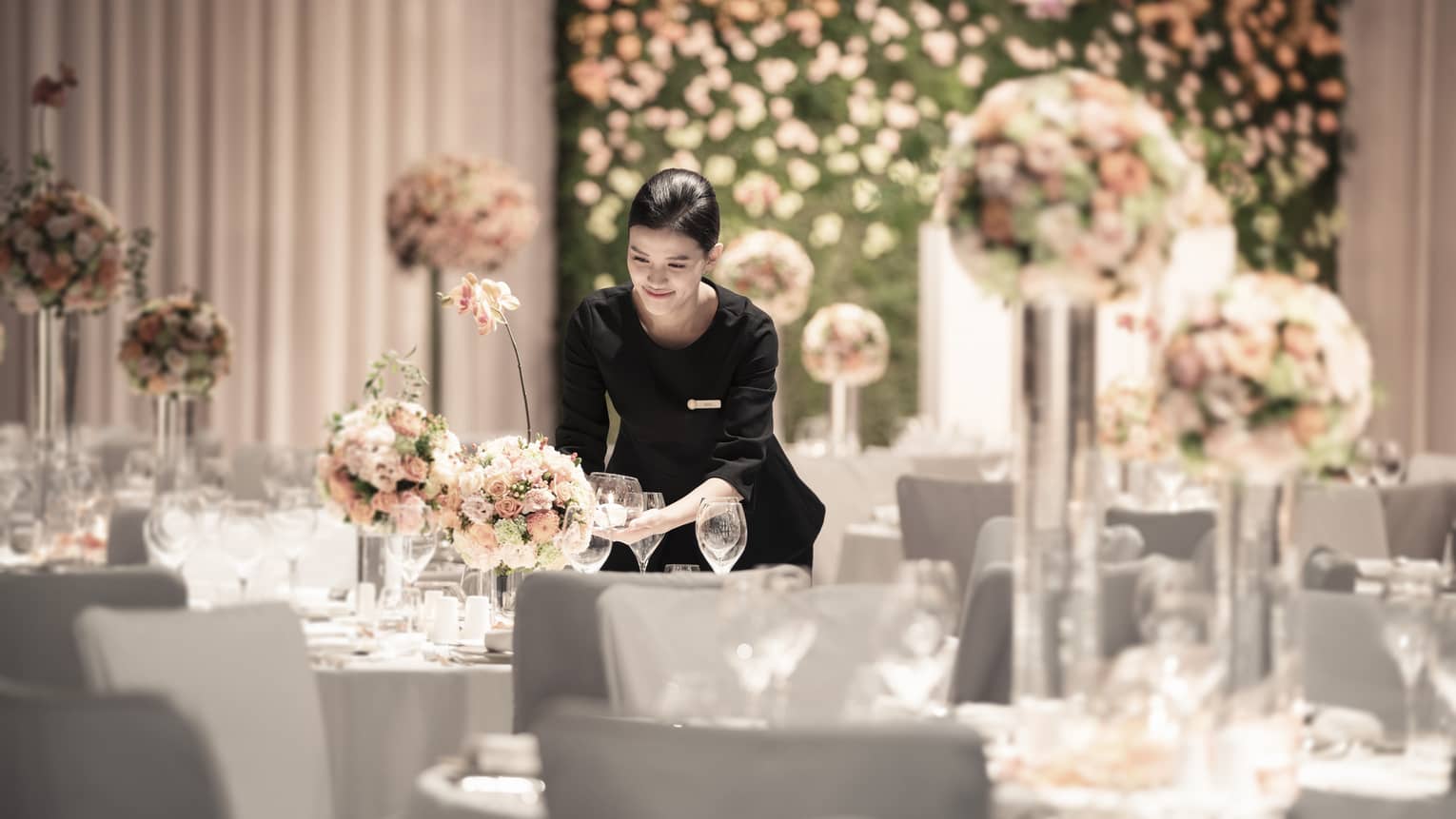 Female staff sets wine glasses on table decorated with bouquets of pastel coloured flowers 