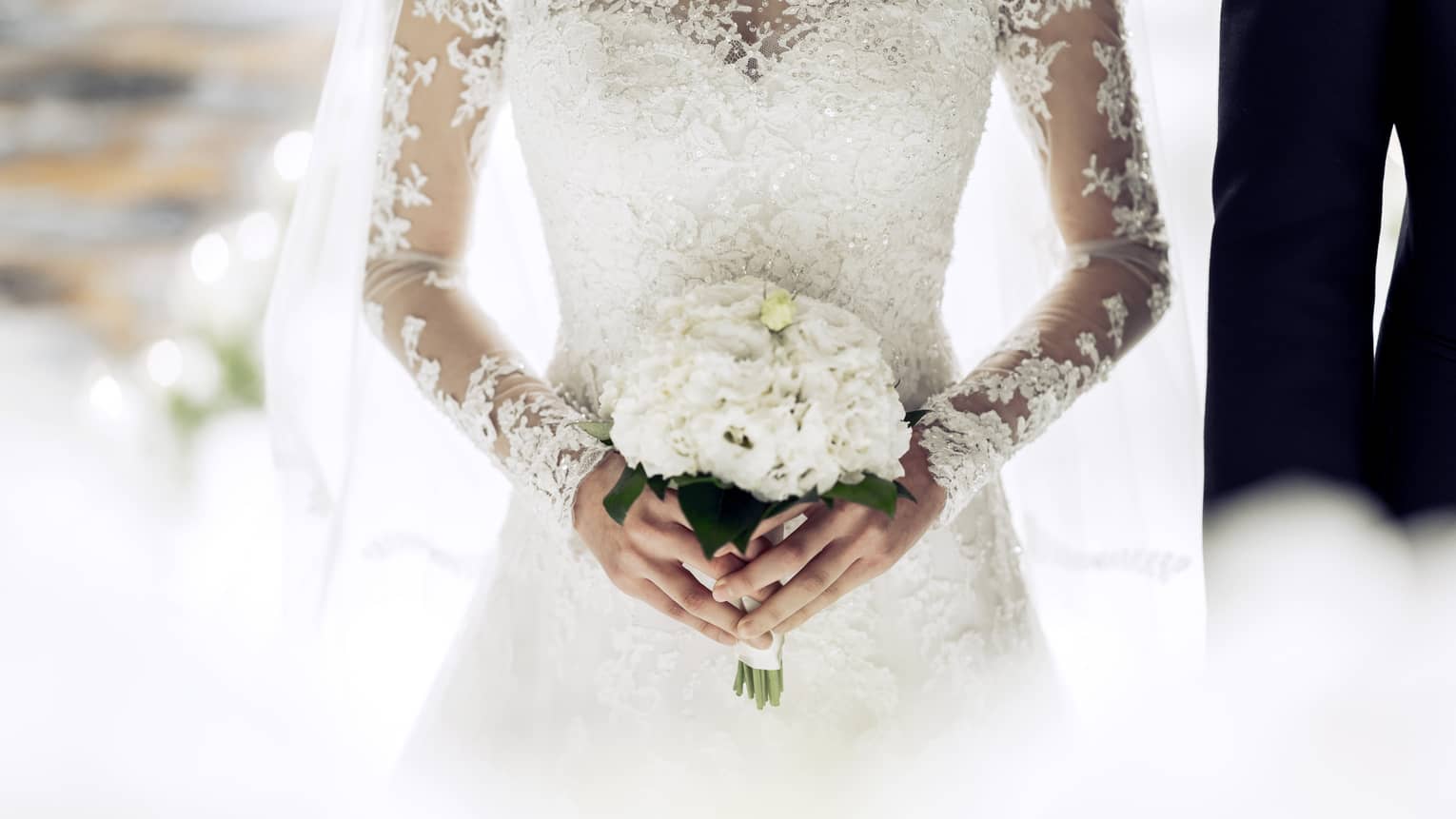 Close up of bride wearing white lace wedding gown and holding bouquet