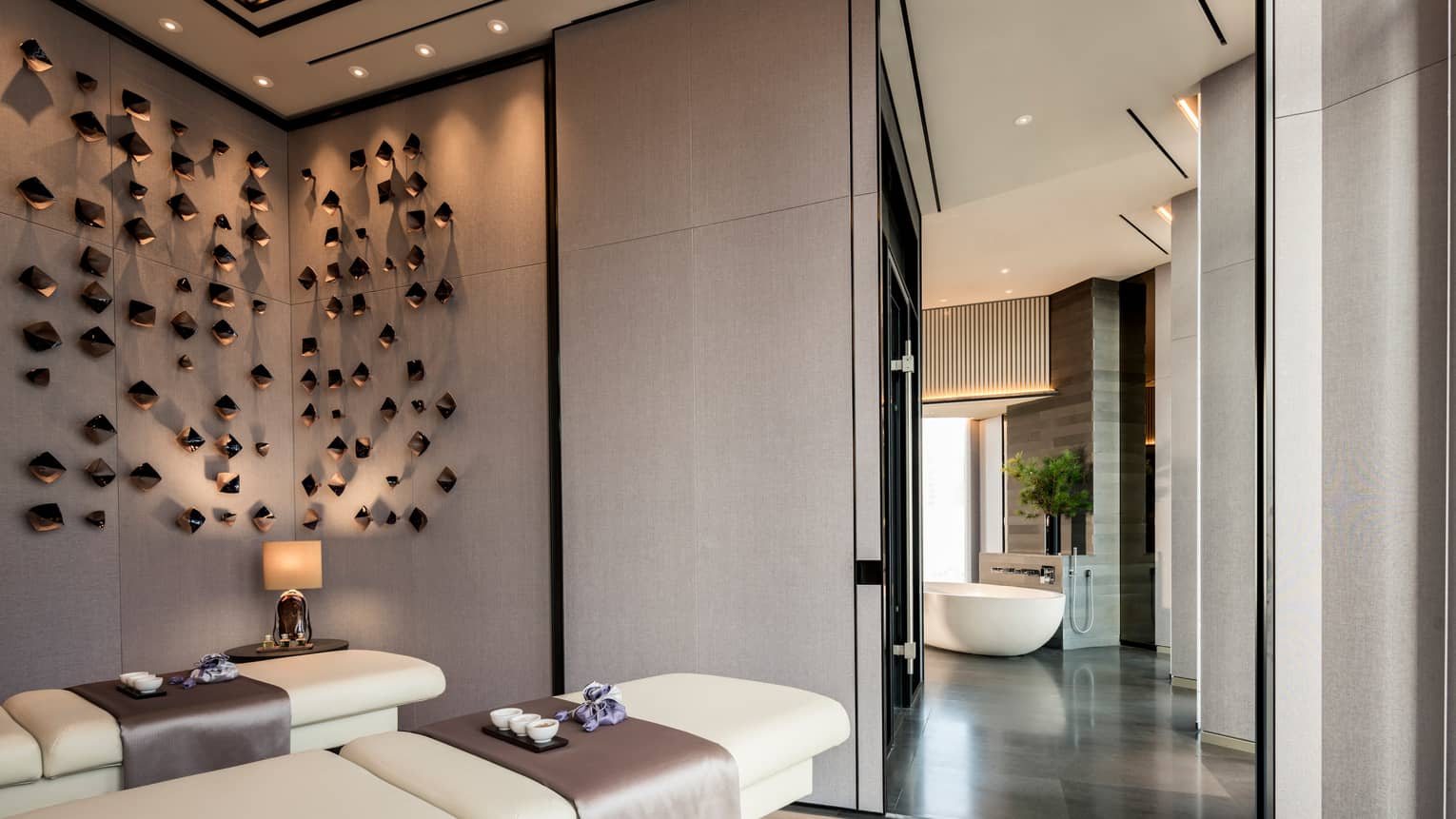 Couples massage beds under modern wall sculptures by hall leading to spa tub