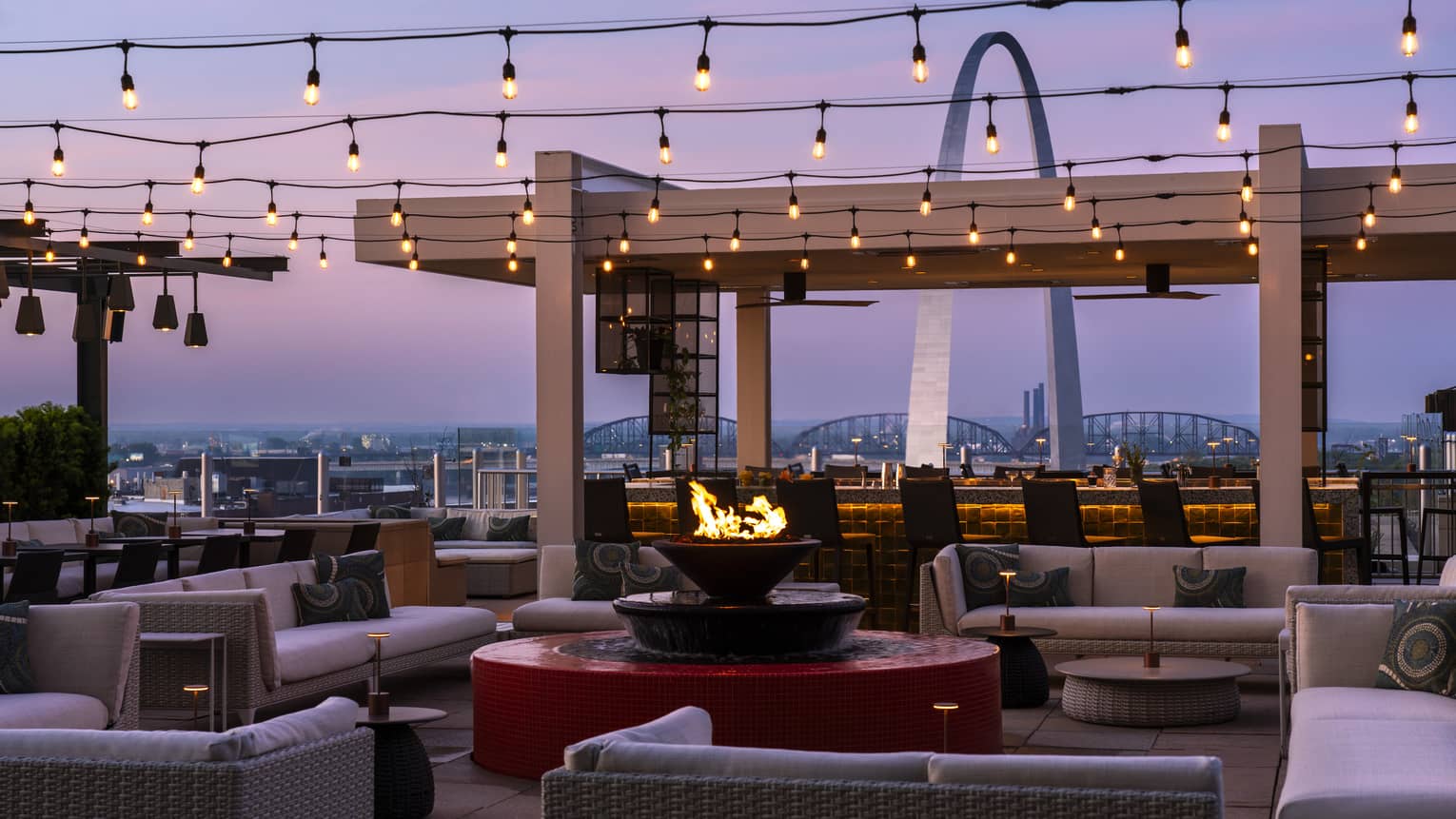 Outdoor lounge with sofas, firepit, string lights and view of St. Louis arch