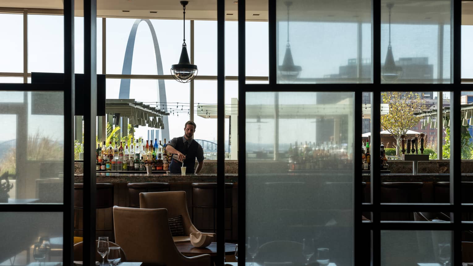 Looking through glass windows at cinderhouse reveals a bartender shaking up a drink at the bar 