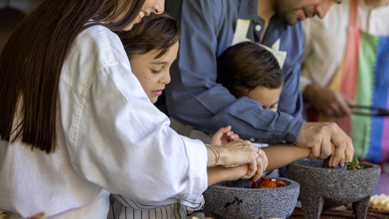 Two adult guests helping two young guests cook.