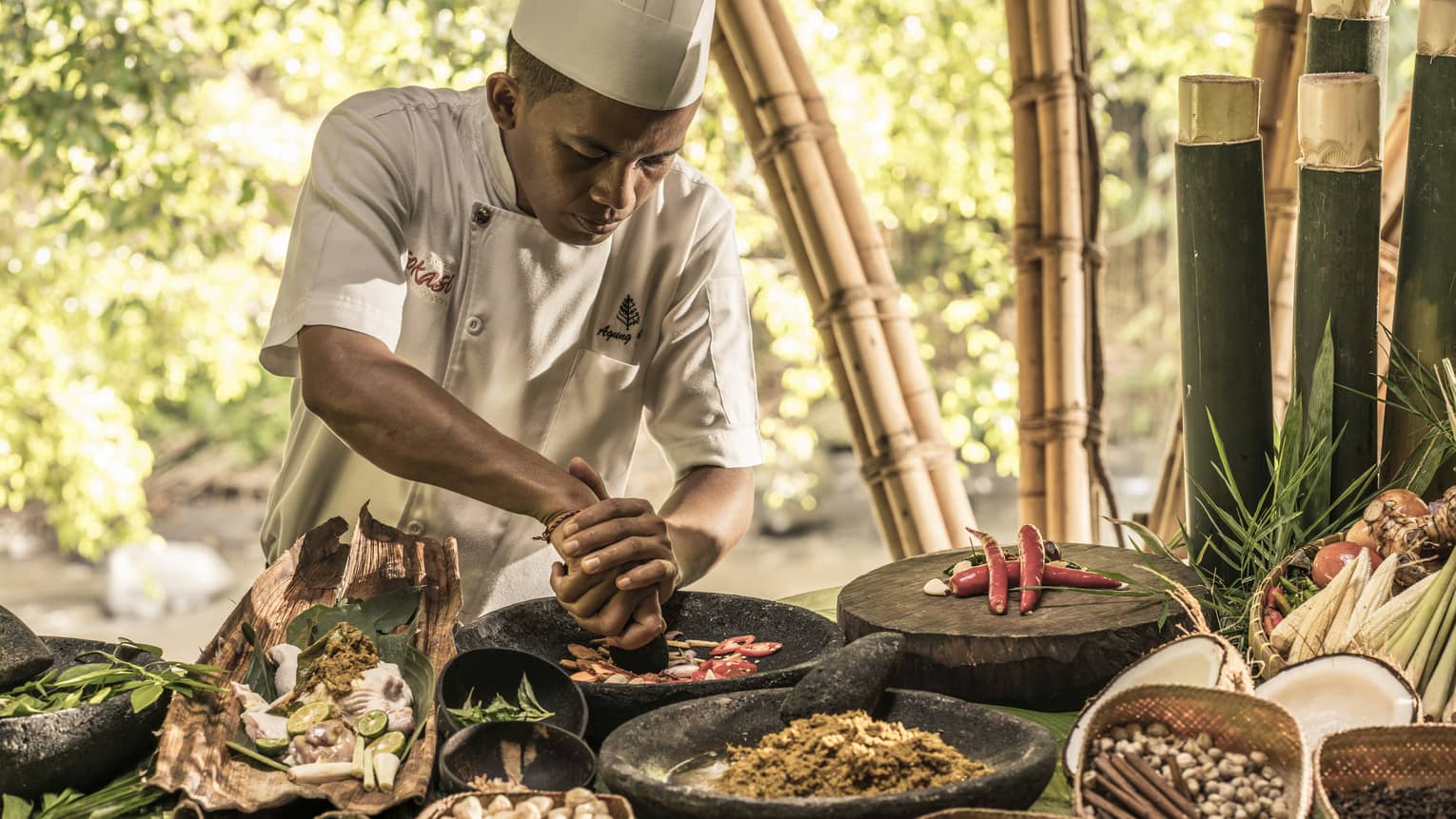 Chef crushes spices and herbs in stone dish on outdoor table