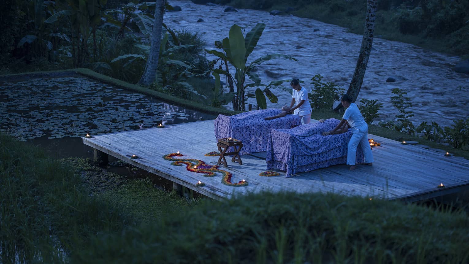Two guests receive candle-lit massages on a dock at night 