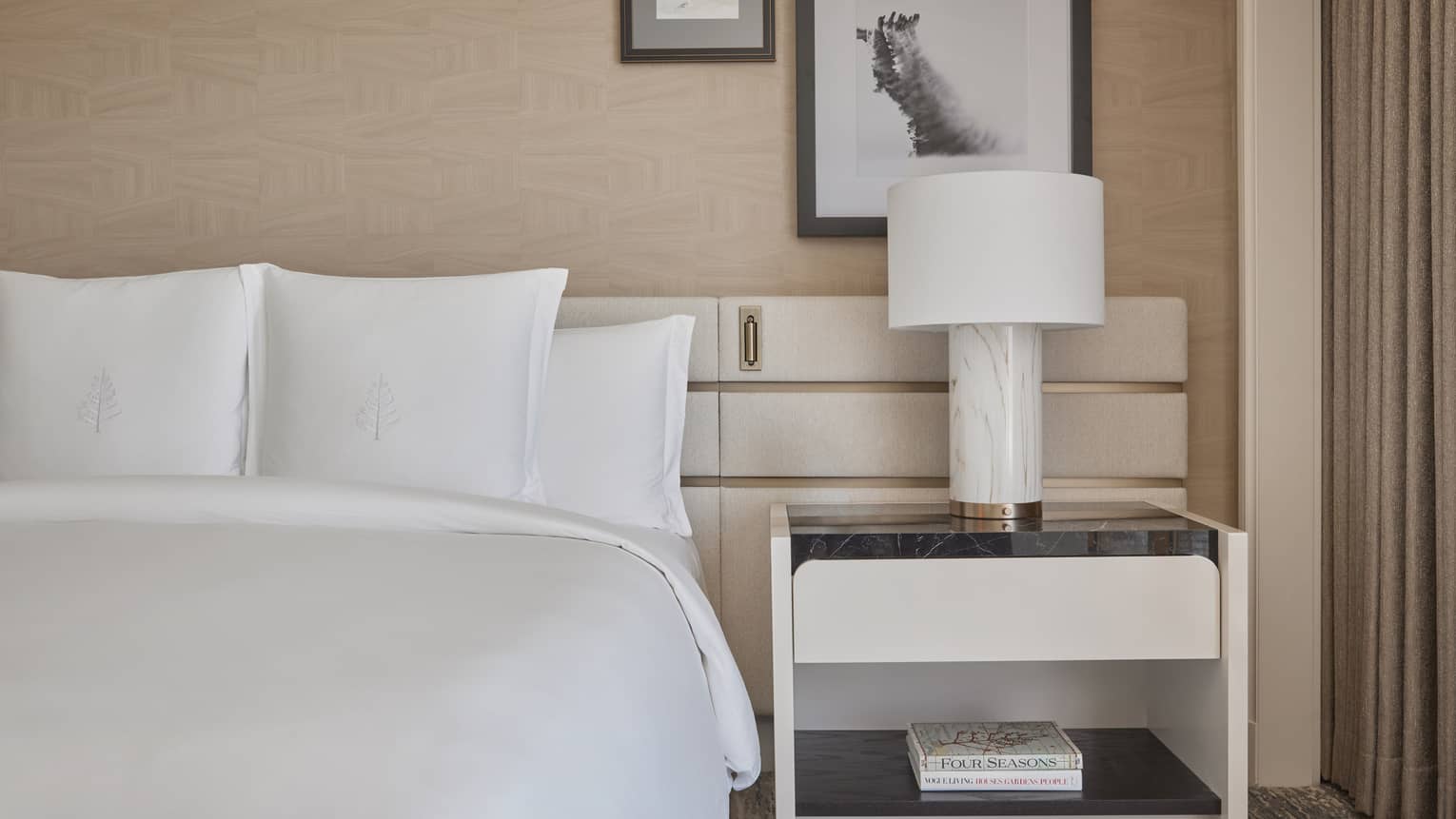 A bed in a guest room with a side table and lamp.
