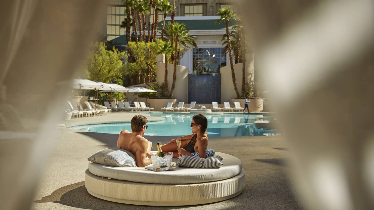 A man and woman lounging on a round daybed near a pool.