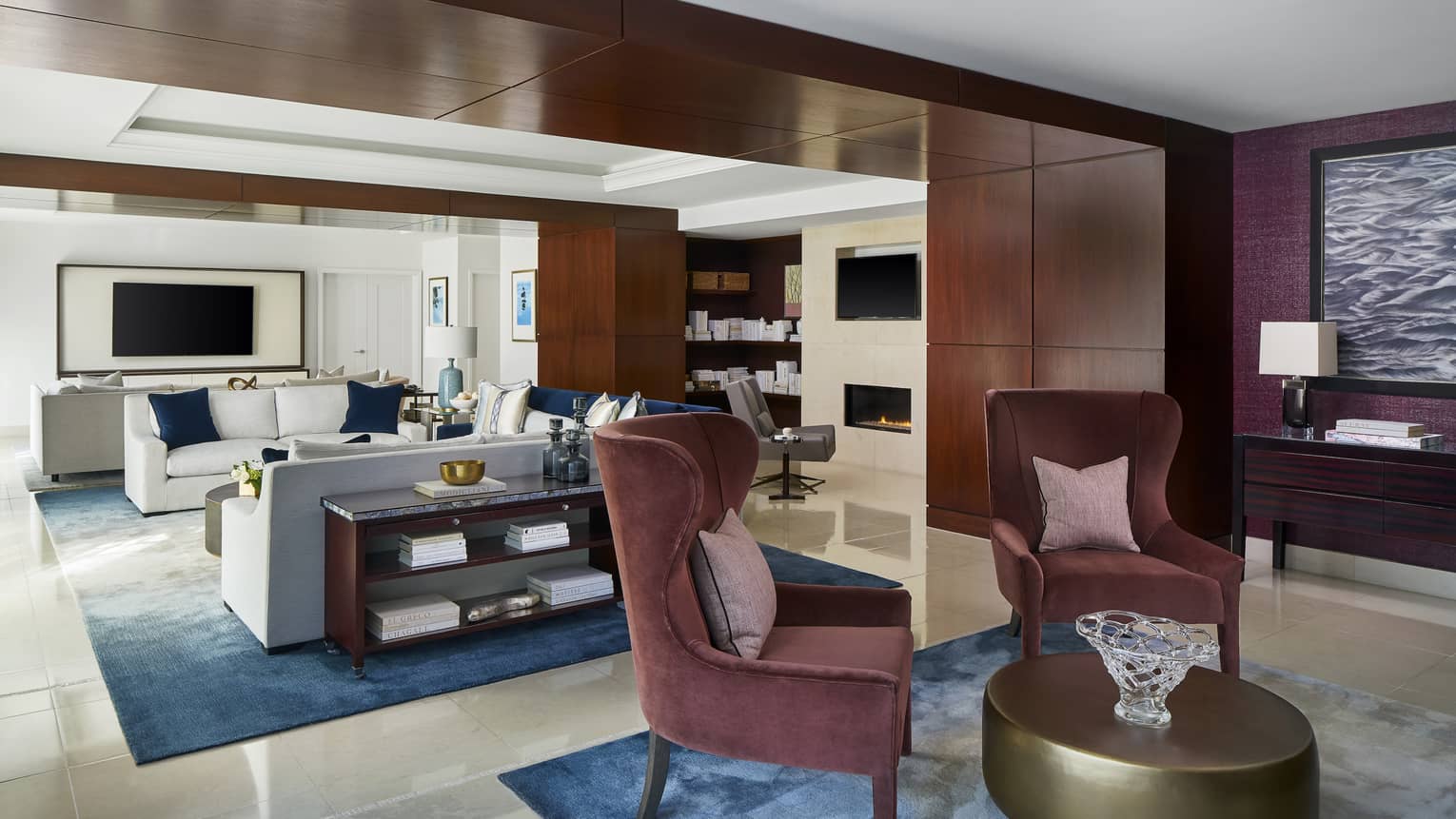 Sitting room with two maroon upholstered chairs, gold circular coffee table, connecting to light-filled living room
