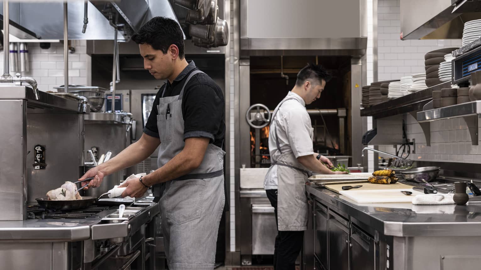 Two chefs wearing aprons are preparing food in an industrial kitchen.