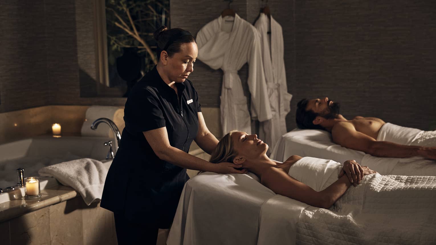 Two guests laying on massage tables in a room with a spa tub.