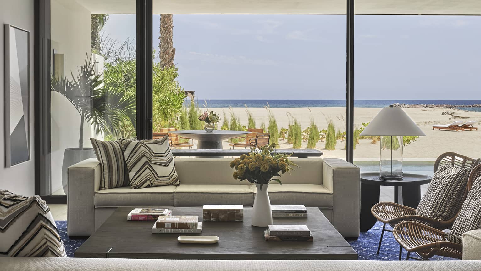Two Bedroom Sunrise Suite living area with cream sofas, blue area rug and floor-to-ceiling windows with ocean views