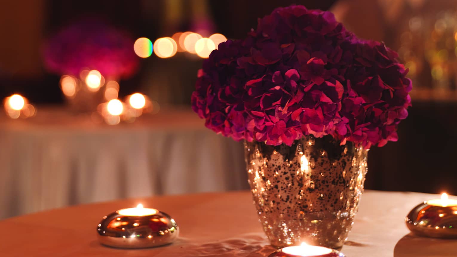 Silver vase of purple hydrangeas on round table surrounded by silver candles