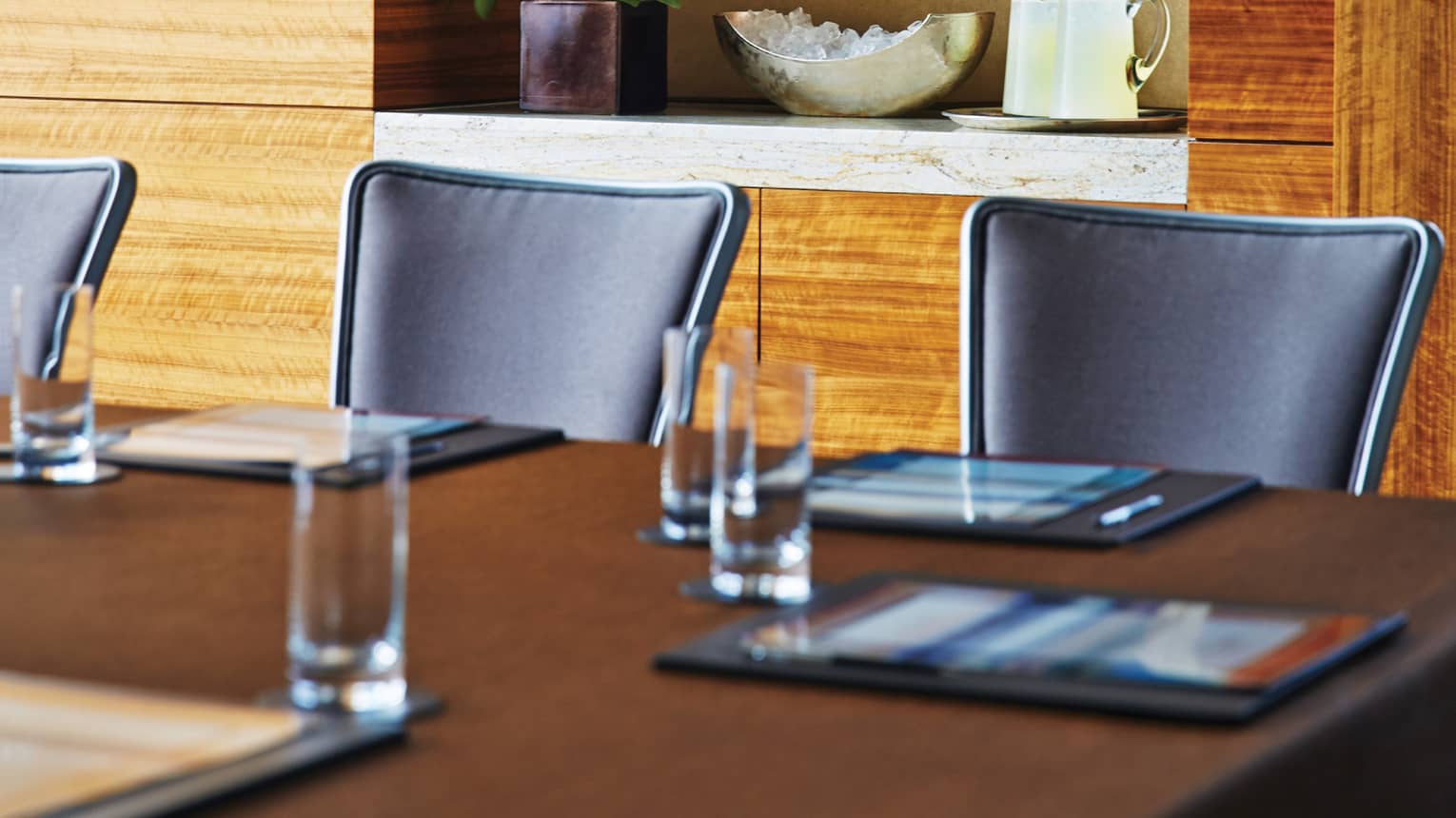 Boardroom table and black meeting chairs in front of modern wood wall, shelf with plant and jugs