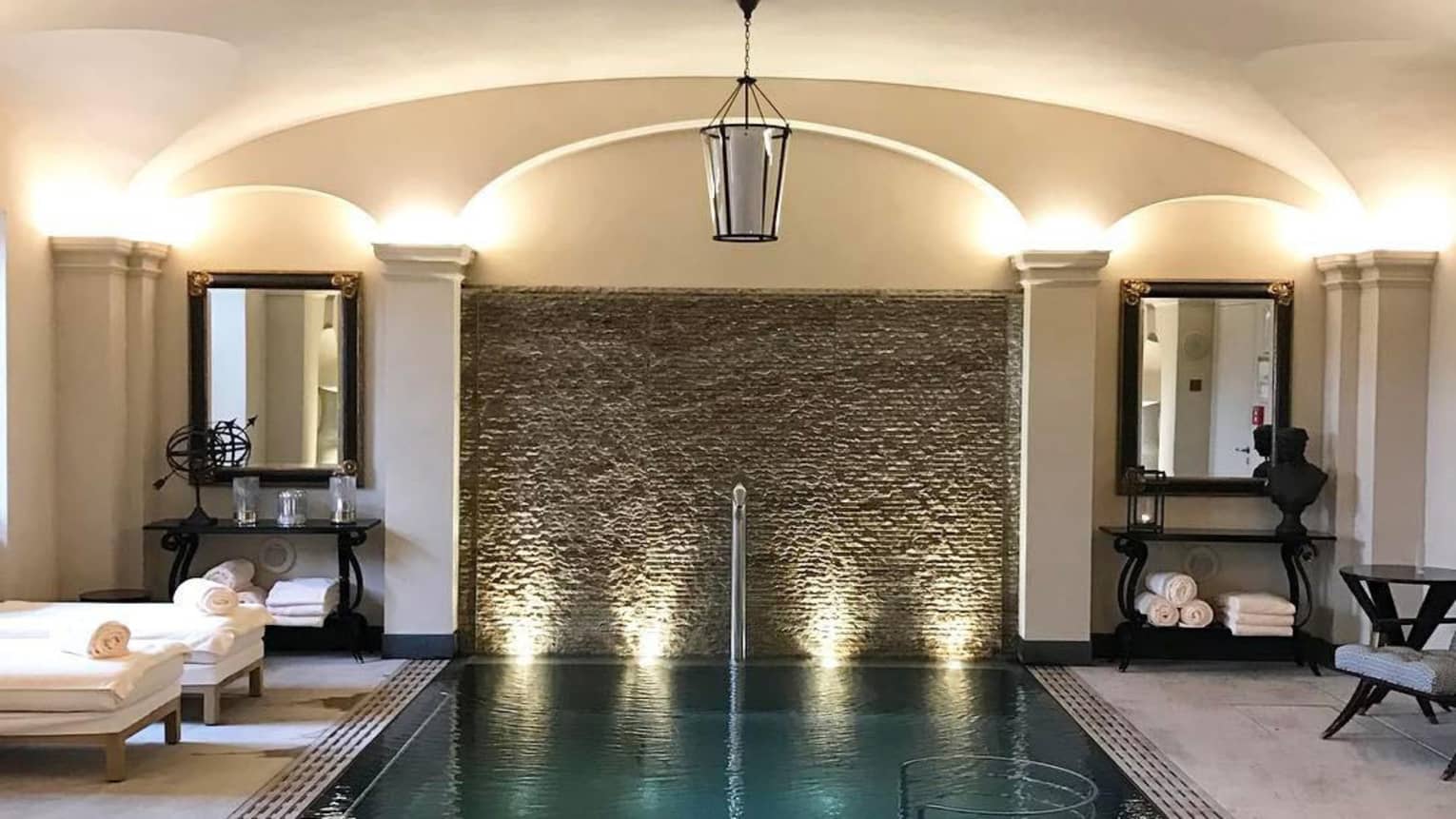 Lantern hangs over Vitality spa pool with white lounge chairs on side, rolled white towels under mirrors
