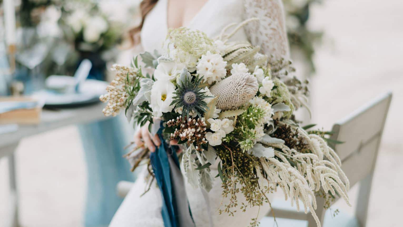 Bride wearing white lace wedding dress holds large floral bouquet