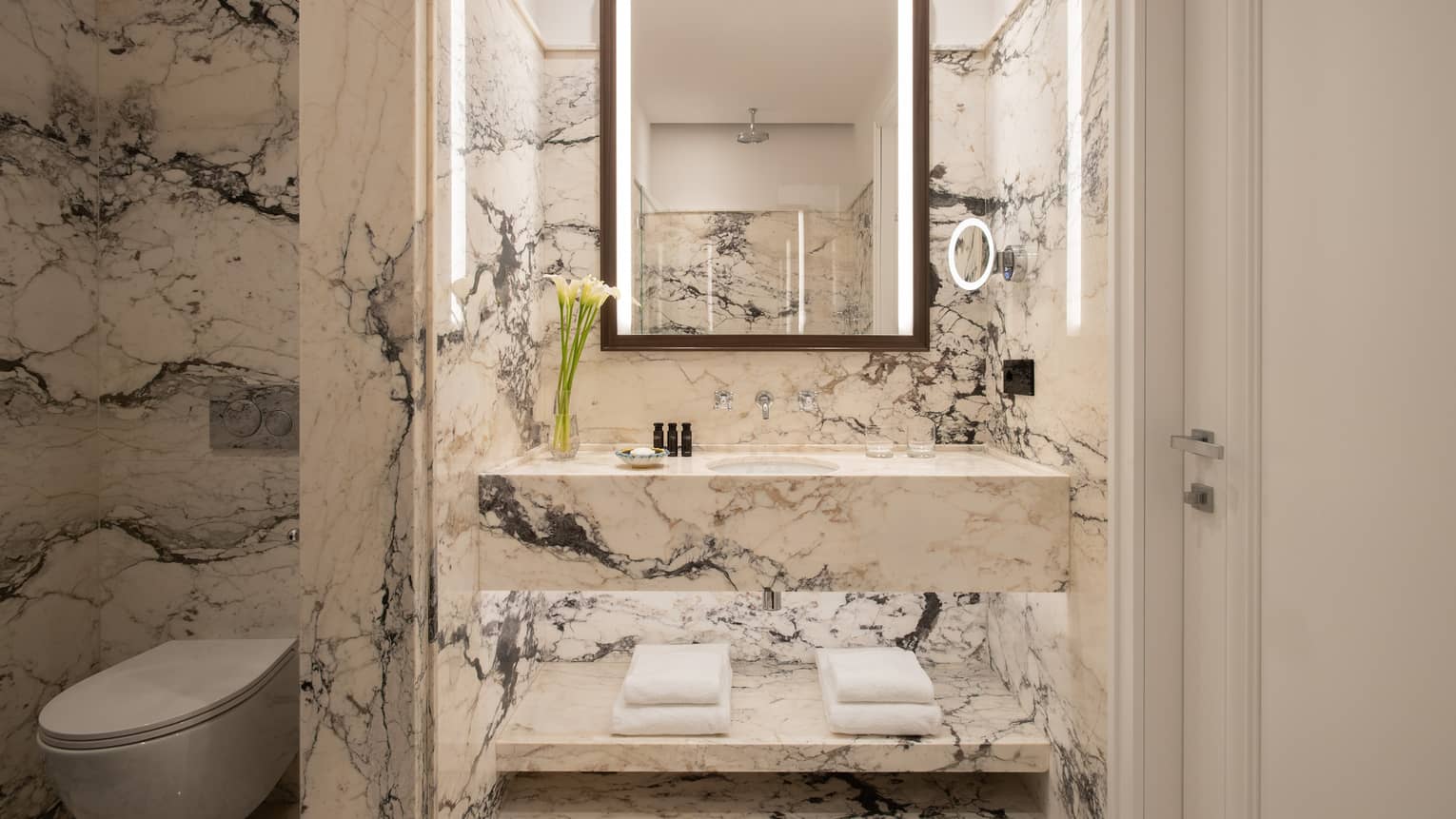 Bathroom with black and white marble walls and vanity, illuminated mirror, separated toilet room