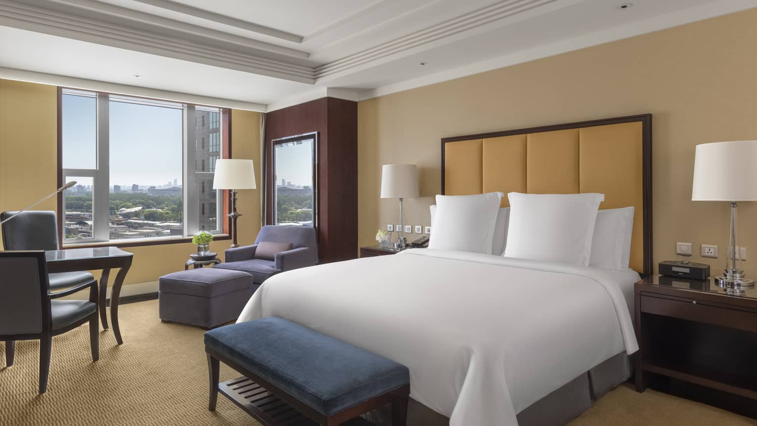 Hotel room with king bed, leather headboard, tan walls and carpet, window, arm chair