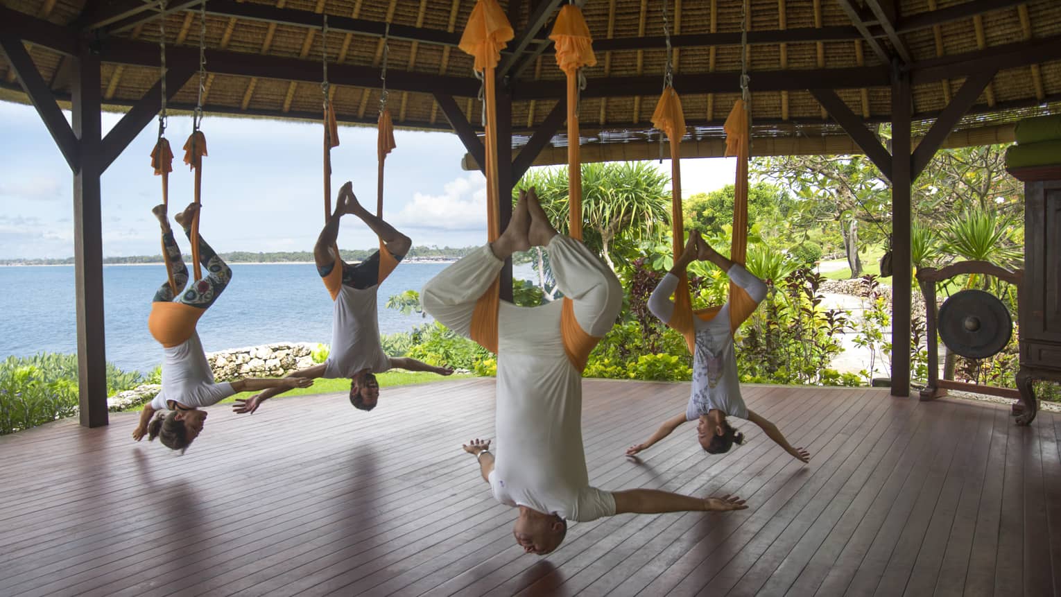 Guests participating in rope yoga, stretching as they are supported by the ceiling of an outdoor pavilion